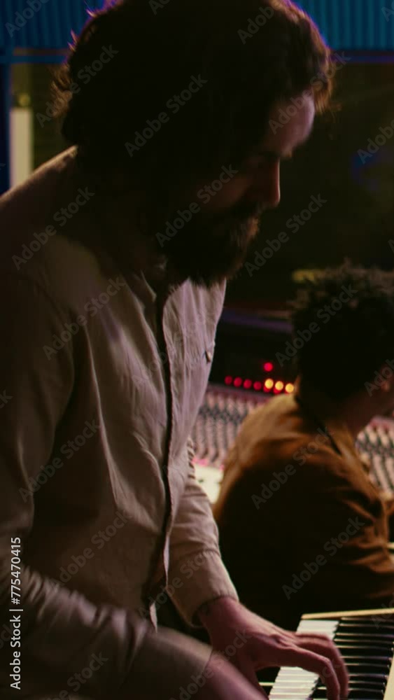 Vertical Video Musician artist playing midi controller synthesizer in recording music studio, composing tracks on mixing console. Singer performing on piano electronic keyboard in control room. Camera Vertical Video Musician artist playing midi controller synthesizer in recording music studio, composing tracks on mixing console. Singer performing on piano electronic keyboard in control room. Camera