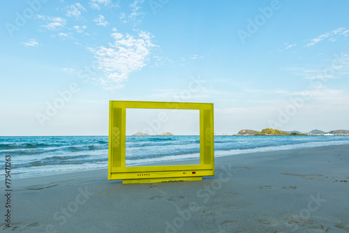 Yellow TV frame on the beach. The blue sky is bright and calm.