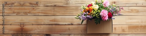 A bright assortment of flowers presented in a cardboard box rests on a wooden surface. Flower delivery concept. Banner. Copy space.