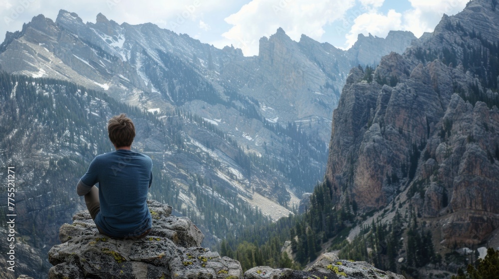 A man sits on a rock face hidden from view as contemplates the majesty of the towering mountain ahead of him. . .
