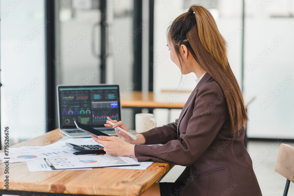 Professional businesswoman examines complex financial data on a laptop screen, with analytical charts spread on the table. Professional businesswoman examines complex financial data on a laptop screen, with analytical charts spread on the table.