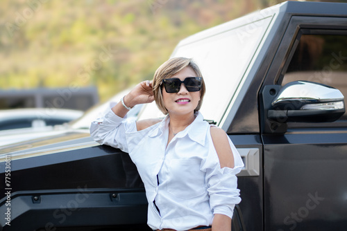 Asian middle-aged in white shirt wears black eyeglasses standing near black big car, soft focus.