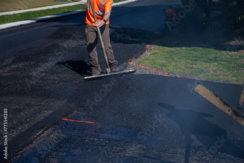 Construction worker with asphalt rake smoothing out fresh blacktop on driveway
