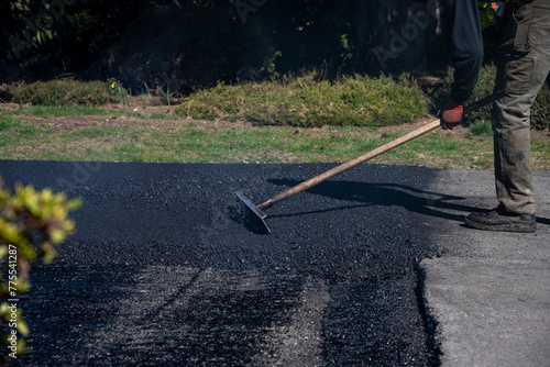 Construction worker with asphalt rake smoothing out fresh blacktop on driveway

