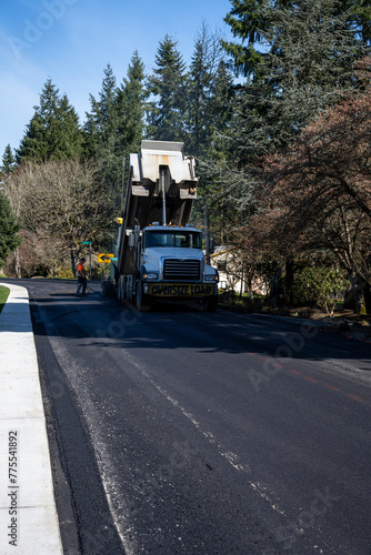 Dump truck with fresh hot asphalt feeding into an asphalt paving machine in the early morning, road re-paving construction project
