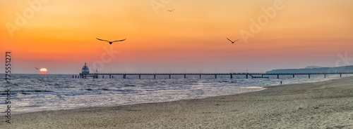 Orangener Sonnenaufgang über der Ostsee Seebrücke Zinnowitz auf Usedom, mit Möwen im Flug über dem Meer.