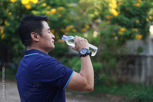 Asian man holds bottle of drinking water to drink outdoor. Concept, Drink water for good health. Relief from thirsty, and protect from heat stroke, cool down in hot weather condition. Health care. photo