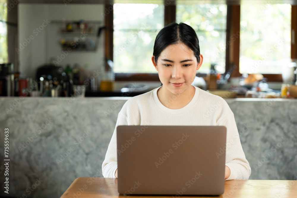 Fototapeta premium Young asian beautiful business woman working with laptop sitting at home. Smiling charming happy young female doing homework meeting conference with team at home.