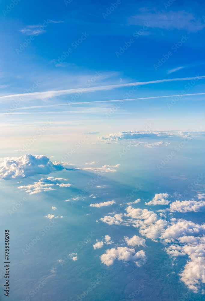 Fototapeta premium Aerial view from airplane window above green ground. View from the airplane window with beautiful clouds at sunrise