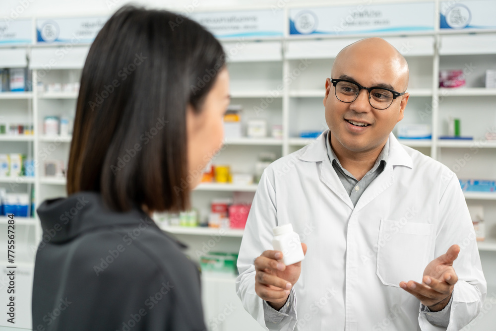 Pharmacist recommends medicines to customers. Asking the questions of medication. Professional Asian male pharmacist giving prescription medications to female patient customers at drugstore shelves. Pharmacist recommends medicines to customers. Asking the questions of medication. Professional Asian male pharmacist giving prescription medications to female patient customers at drugstore shelves.