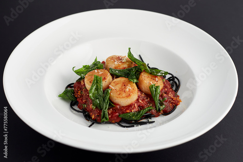 Black spaghetti Arrabbiata sauce with scallop served in white plate isolated on black background. italian food.