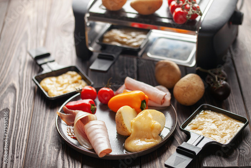 Fototapeta Naklejka Na Ścianę i Meble -  Delicious traditional Swiss melted raclette cheese on diced boiled or baked vegetables served in individual skillets