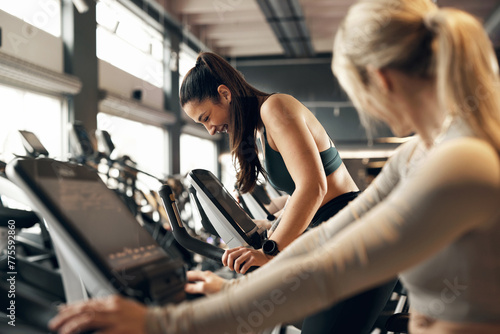 Fit young woman and a group of female friends in sportswear laughing while riding stationary bikes during a cardio workout session together in a health club photo