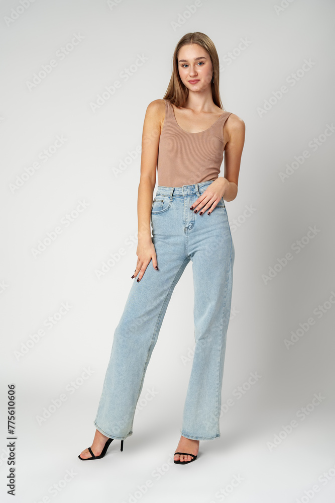 Young Woman Wearing High Rise Jeans and Tank Top posing on gray background in studio Young Woman Wearing High Rise Jeans and Tank Top posing on gray background in studio