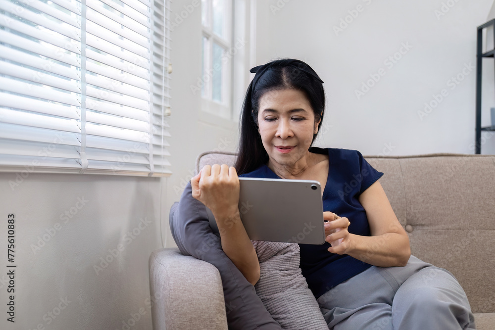 Elderly woman's leisure day watching social media on tablet, watching news on sofa in living room Elderly woman's leisure day watching social media on tablet, watching news on sofa in living room
