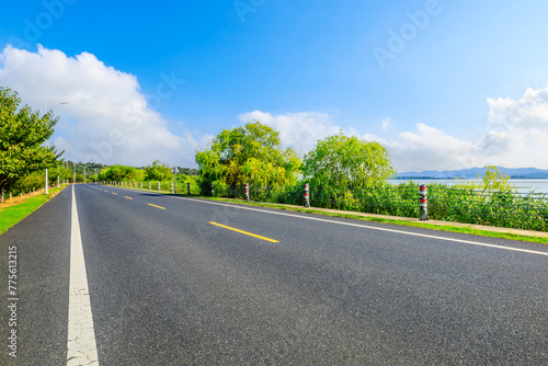 Country road and green trees with beautiful sky clouds by the lake