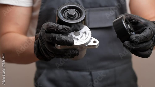 An auto mechanic holds in his hands in black gloves a idler pulley with a tensioner for a car's poly V-belt and a parasitic roller, close-up. Auto parts replacement concept, car maintenance photo