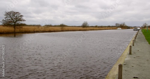 Speeded up shot looking up the river Bure with a white Norfolk Broads cruisers boat passing moored boats photo