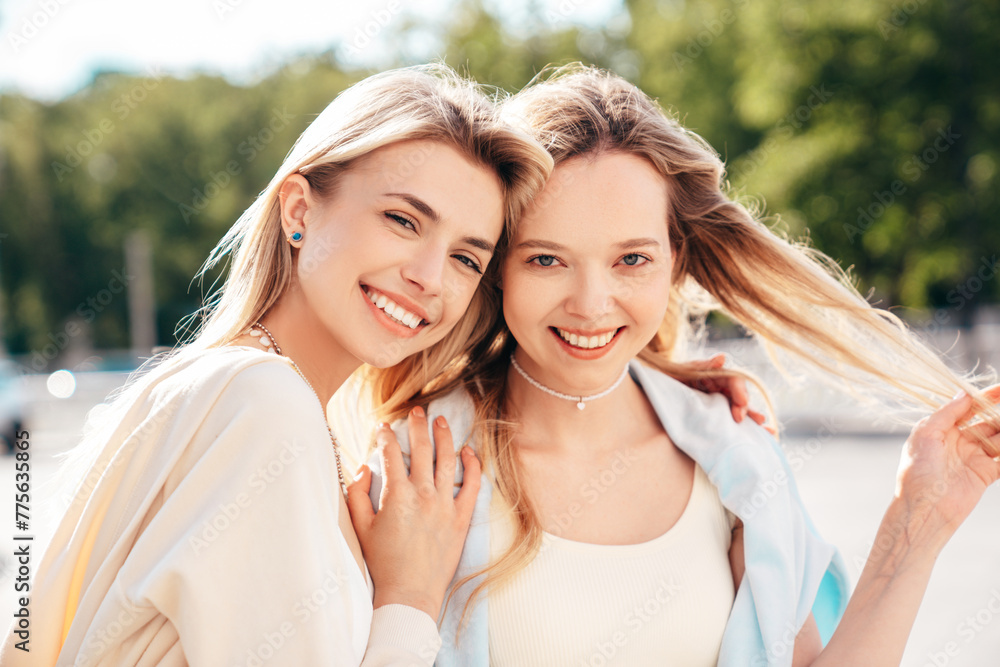 Two young beautiful smiling blond hipster female in trendy summer clothes. Sexy carefree women posing on street background. Positive models having fun, hugging at sunset. Cheerful and happy