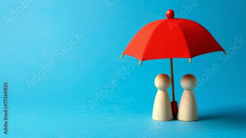 Red toy umbrella and wooden doll figures isolated on a blue background. Insurance coverage concept