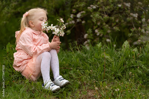 Little girl in pink dress in the garden. Girl sitting with blooming branch and snuffles their. Spring day