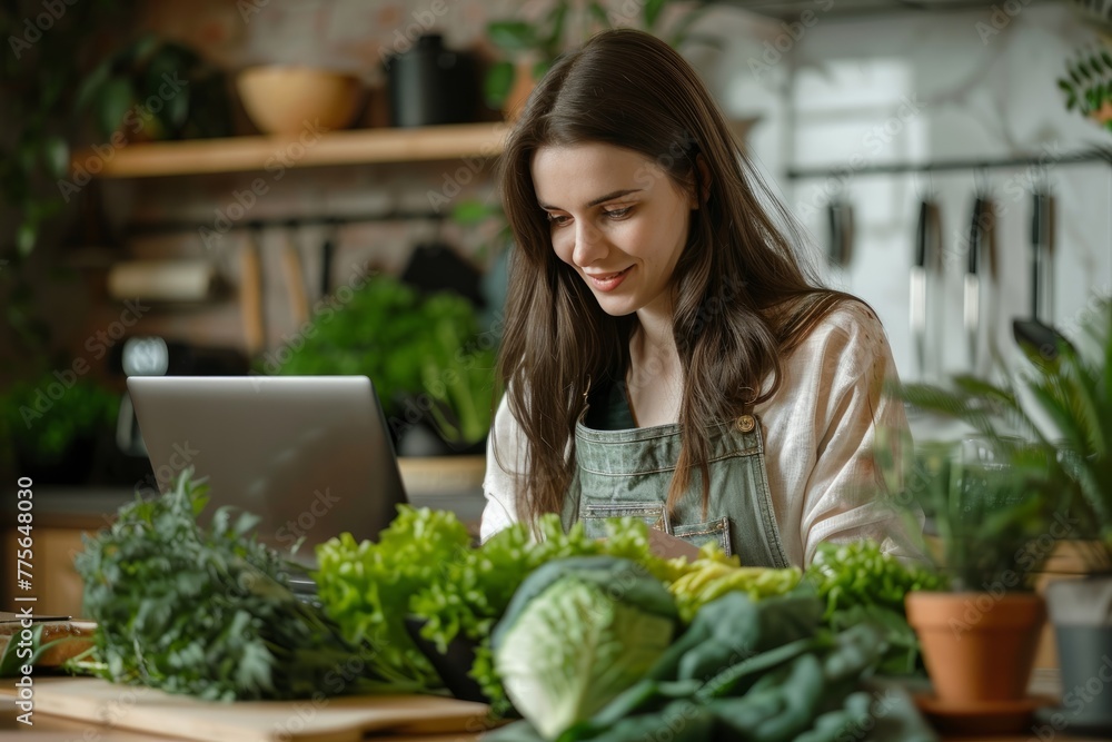 A Young Woman Sits With A Laptop At Her Kitchen Table Surrounded By Greens And Vegetables. Concept Paleo Diet
