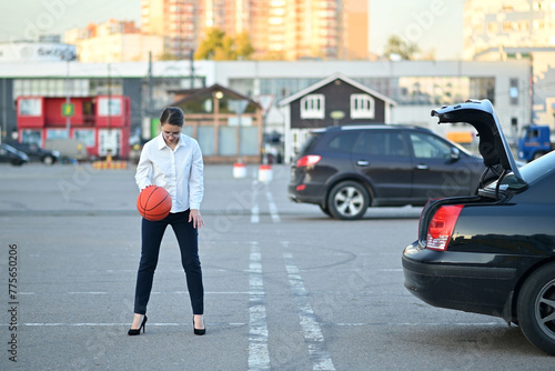 young woman in formal office clothes plays with a basketball in the parking lot © Вячеслав Думчев