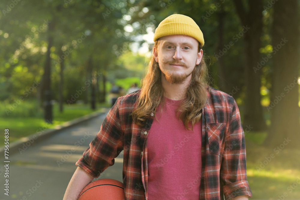 Portrait of a young red-haired guy in a yellow hat with a basketball