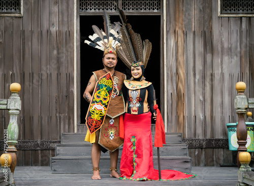 Portrait of man and woman wearing traditional Kalimantan Dayak clothing with the background of a traditional Dayat house called 