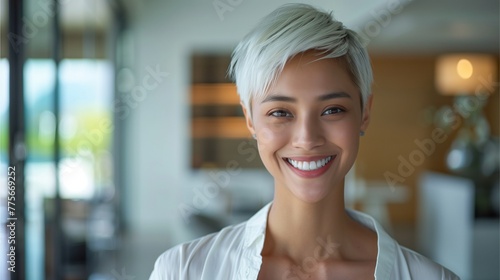 Thai woman with short white hair smiling. The backdrop is the interior of a modern home.