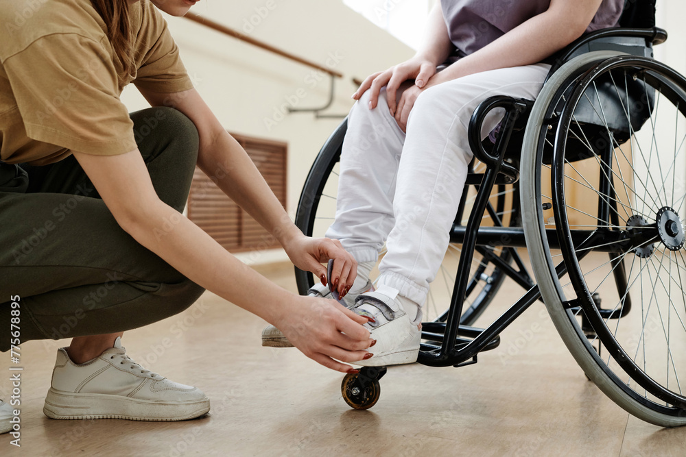 Obraz premium Crop shot of unrecognizable dance coach helping woman in wheelchair to fix shoes on her feet