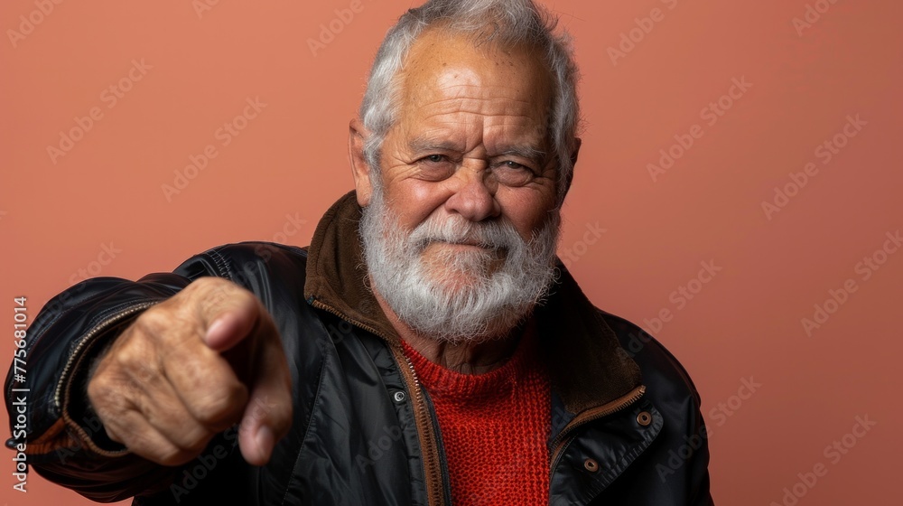 Bespectacled gray-haired man showing the direction using a hand gesture on pink background