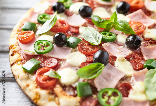 Pizza with ham, mozzarella cheese, cherry tomatoes, green and jalapeno pepper, black olives and fresh basil. Bright background. Close up. 