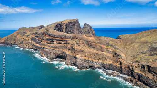 The rocky coastline with a light blue sea, rocks, and green hills. It's a sunny day. PR8 trail in Madeira. It looks like a beautiful coastal landscape.