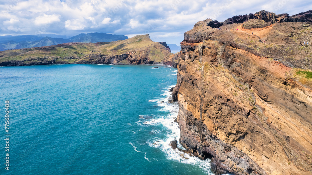 The rocky coast of Madeira, with green cliffs rising above the blue ocean. Waves gently crash against the base of the cliffs, creating white foam. The sky is almost clear with a few clouds.
The rocky coast of Madeira, with green cliffs rising above the blue ocean. Waves gently crash against the base of the cliffs, creating white foam. The sky is almost clear with a few clouds.