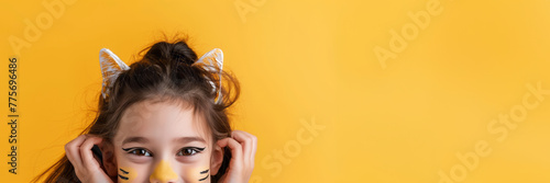 Cheerful child with kitty face make-up on yellow background with copy space.