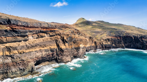 The steep, green cliffs of Madeira above the azure ocean. Mist envelops the peaks, and waves crash against the rocky coastline. It's the beauty of nature and the rugged charm of the island.