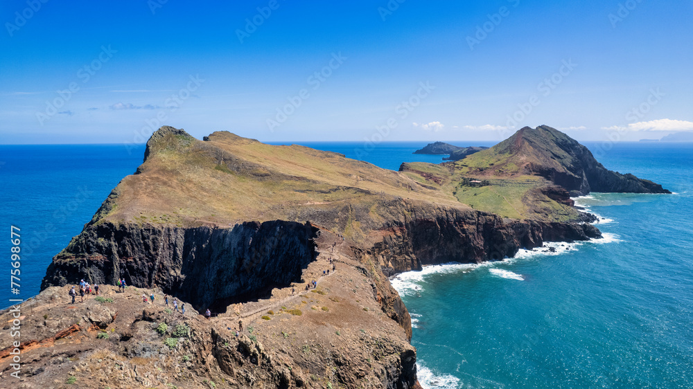 The steep, green cliffs of Madeira above the azure ocean. Mist envelops the peaks, and waves crash against the rocky coastline. It's the beauty of nature and the rugged charm of the island.