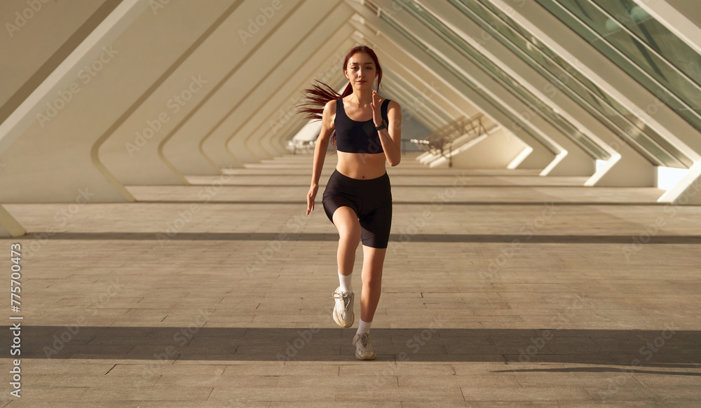 Young sporty female athlete in sportswear running outdoors on a sunny day . Morning jog Young sporty female athlete in sportswear running outdoors on a sunny day . Morning jog