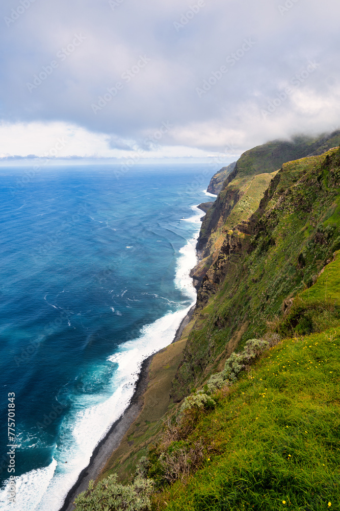The steep, green cliffs of Madeira above the azure ocean. Mist envelops the peaks, and waves crash against the rocky coastline. It's the beauty of nature and the rugged charm of the island. The steep, green cliffs of Madeira above the azure ocean. Mist envelops the peaks, and waves crash against the rocky coastline. It's the beauty of nature and the rugged charm of the island.
