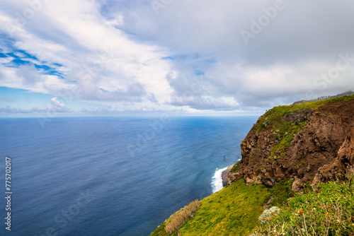 A picturesque coastal landscape in Madeira. Visible are houses surrounded by greenery, mountains, and the azure sea. The harmony of nature and human habitation.
