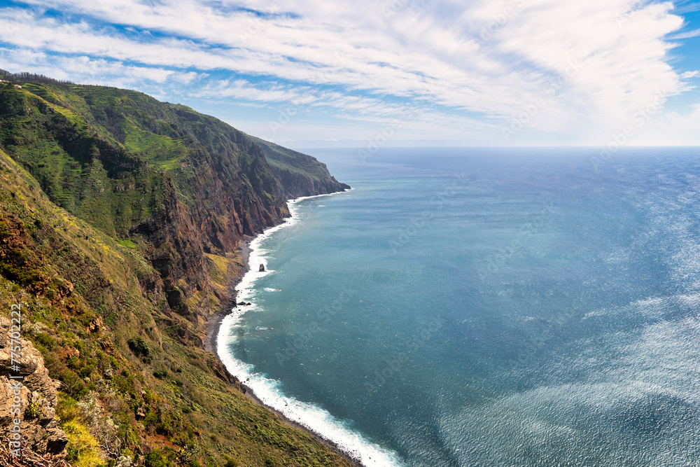The photo depicts a steep, green mountainside in Madeira, sloping down to the blue sea. Waves crash against the rocky coast, and dense clouds dominate the scene, creating an image of untouched nature. The photo depicts a steep, green mountainside in Madeira, sloping down to the blue sea. Waves crash against the rocky coast, and dense clouds dominate the scene, creating an image of untouched nature.