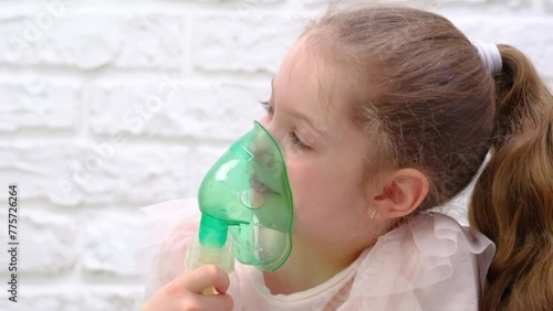 Little girl makes inhalation with medical nebulizer while sitting on bed. Cute child is sick bronchitis or asthma and breathes through inhaler at home
