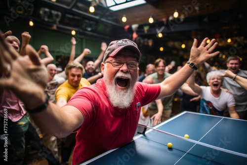 A man with a beard is actively engaged in a game of ping pong, showing focus and skill as he competes. The table tennis fans surrounding the table are watching intently © Vit