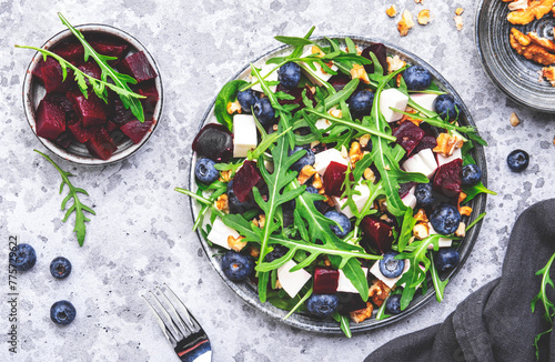 Delicious salad with sweet beets, blueberries, feta cheese, arugula and walnuts, gray table background, top view
