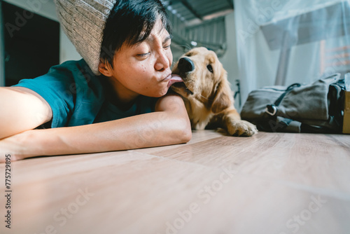 A real Asian man takes a selfie with a 7-month-old golden retriever. The dog is licking its owner's face. People and fun playing together Looking happily at the camera at home