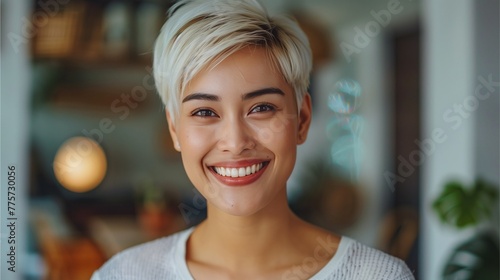 Thai woman with short white hair smiling. The backdrop is the interior of a modern home.