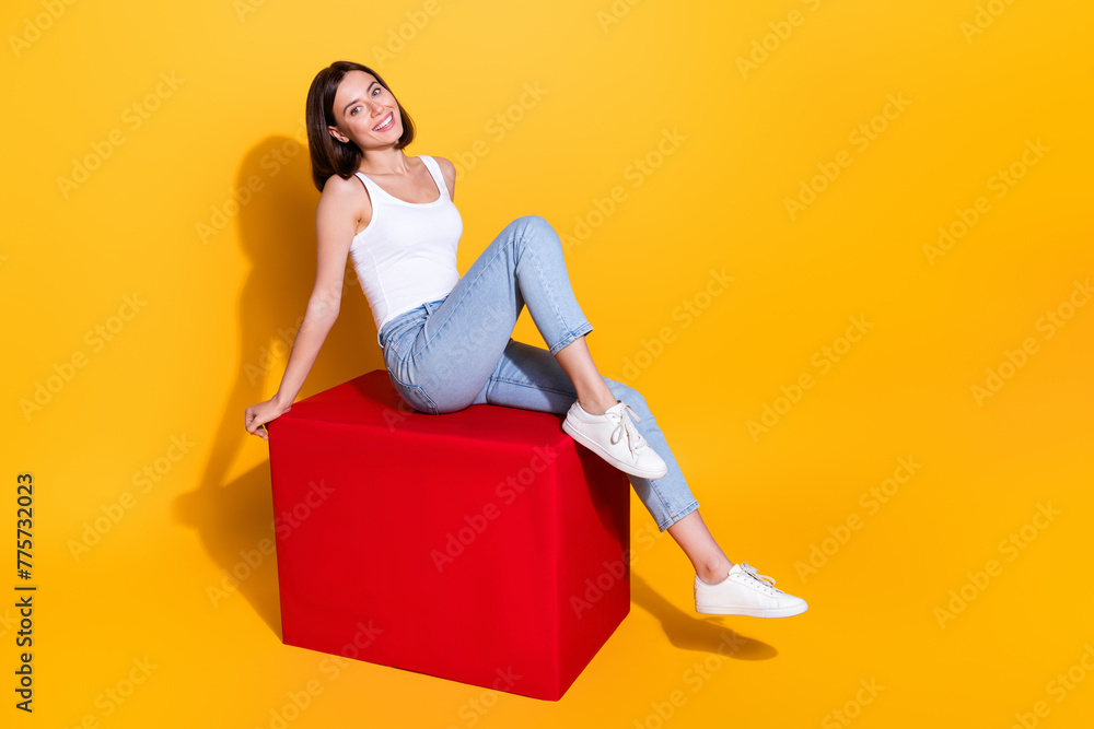 Obraz premium Full length photo of sweet adorable woman wear white singlet sitting red cube empty space isolated yellow color background