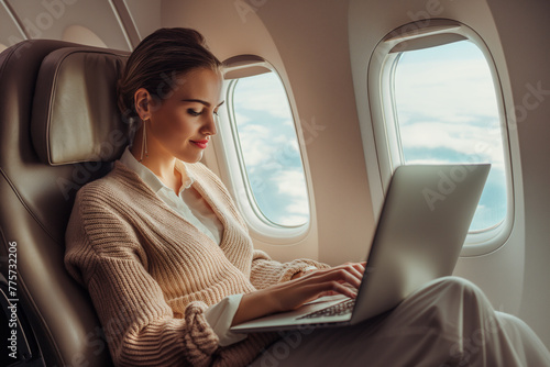 Attractive beautiful young businesswoman passenger of airplane sitting in comfortable seat while working at laptop computer and using wireless connection on board. © ME Image
