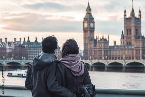 A man and a woman stand near Big Ben in London, gazing out over the water of the River Thames on a sunny day © Jelena